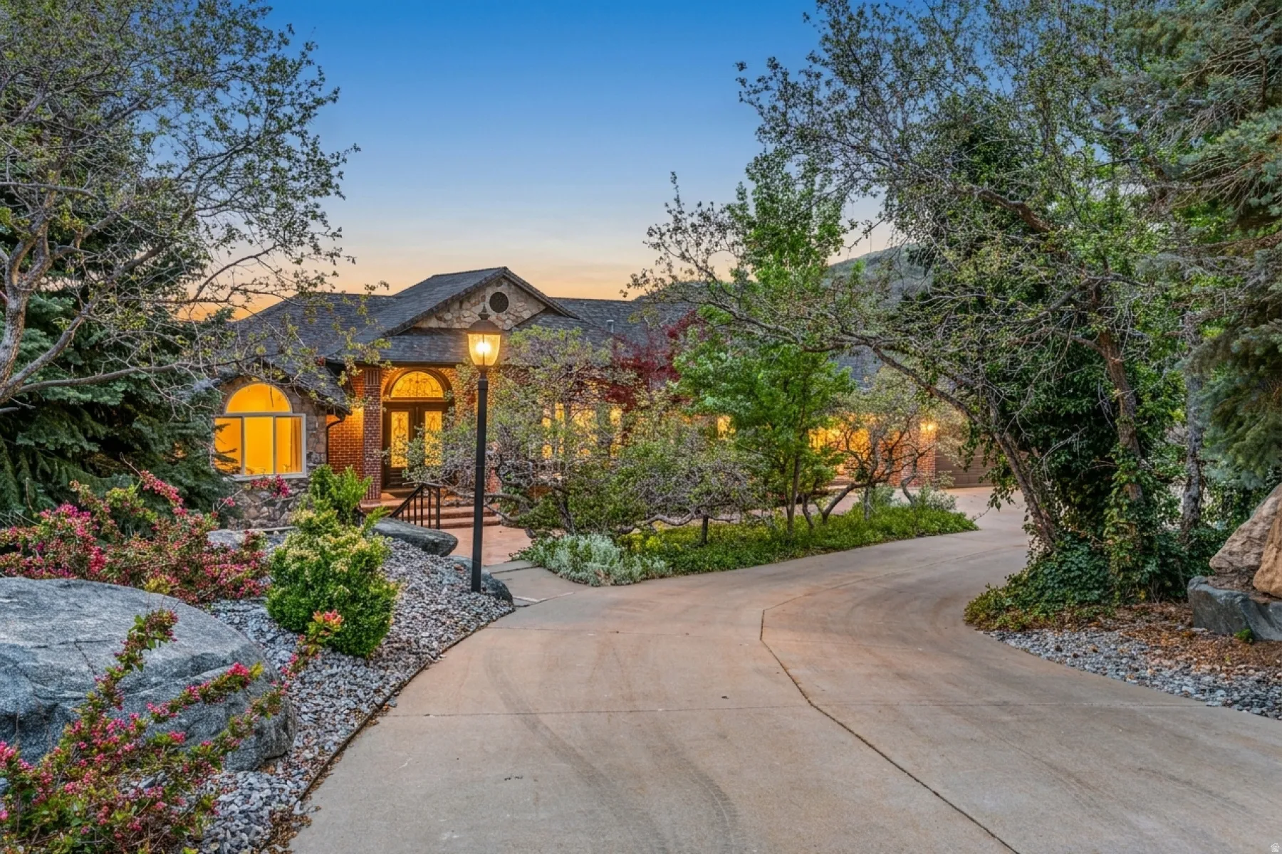 Paved driveway framed by mature trees, leading to a stone and brick facade residence