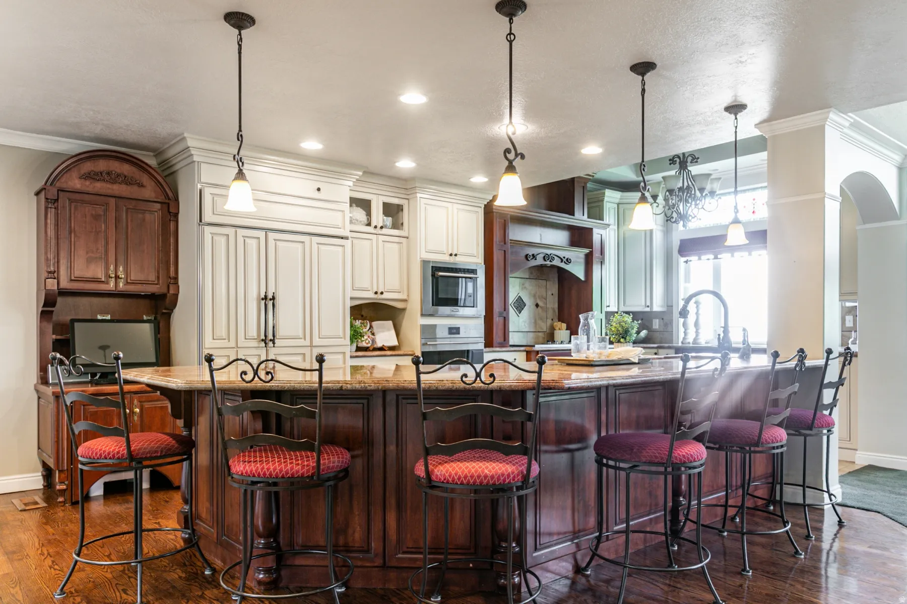 Spacious kitchen island with seating, featuring a stone-finish countertop, dark wood cabinetry, and recessed lighting