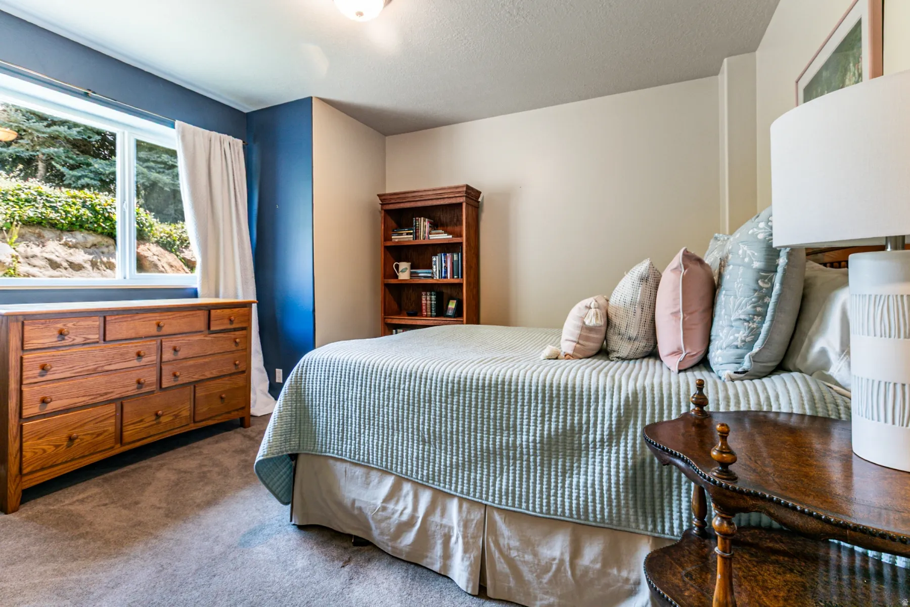 Carpeted room featuring a window with natural light, a wood-finish dresser with multiple drawers, and a built-in wood-finish bookshelf