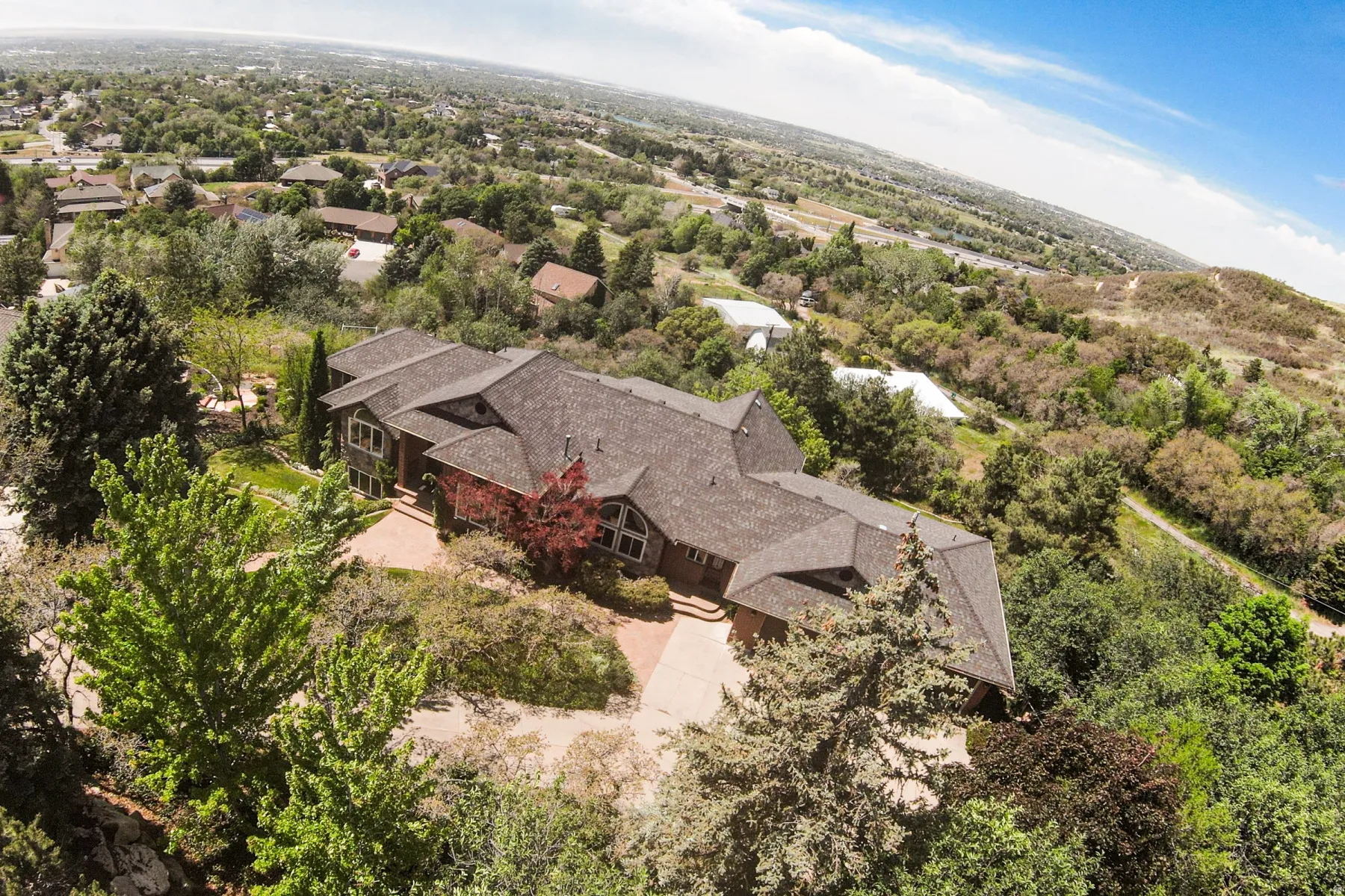 Expansive property featuring a multi-level roofline, extensive natural landscaping, a brick paver driveway, and a natural wood-sided exterior