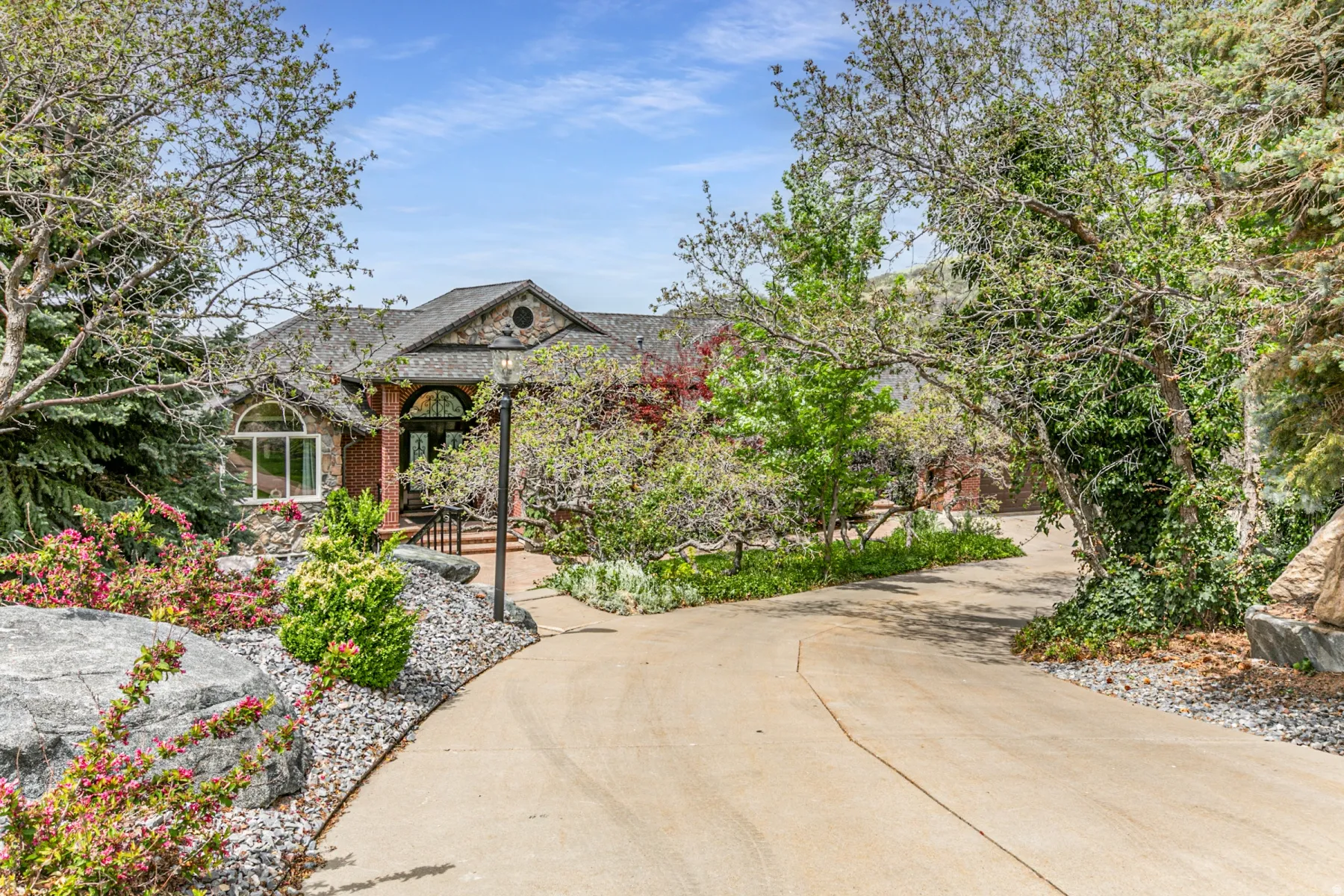 Curved concrete driveway leading to a brick and stone facade residence with an arched entry and a dark shingle roof