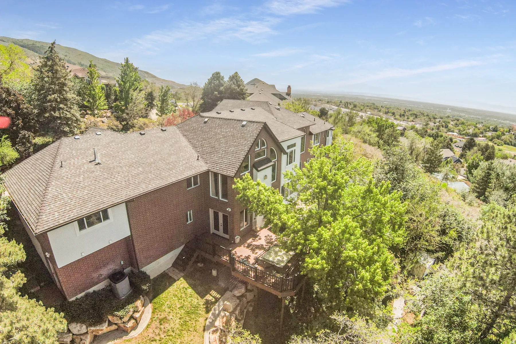 Multi-level brick exterior residence with a shingle roof and a wooden deck featuring a hot tub