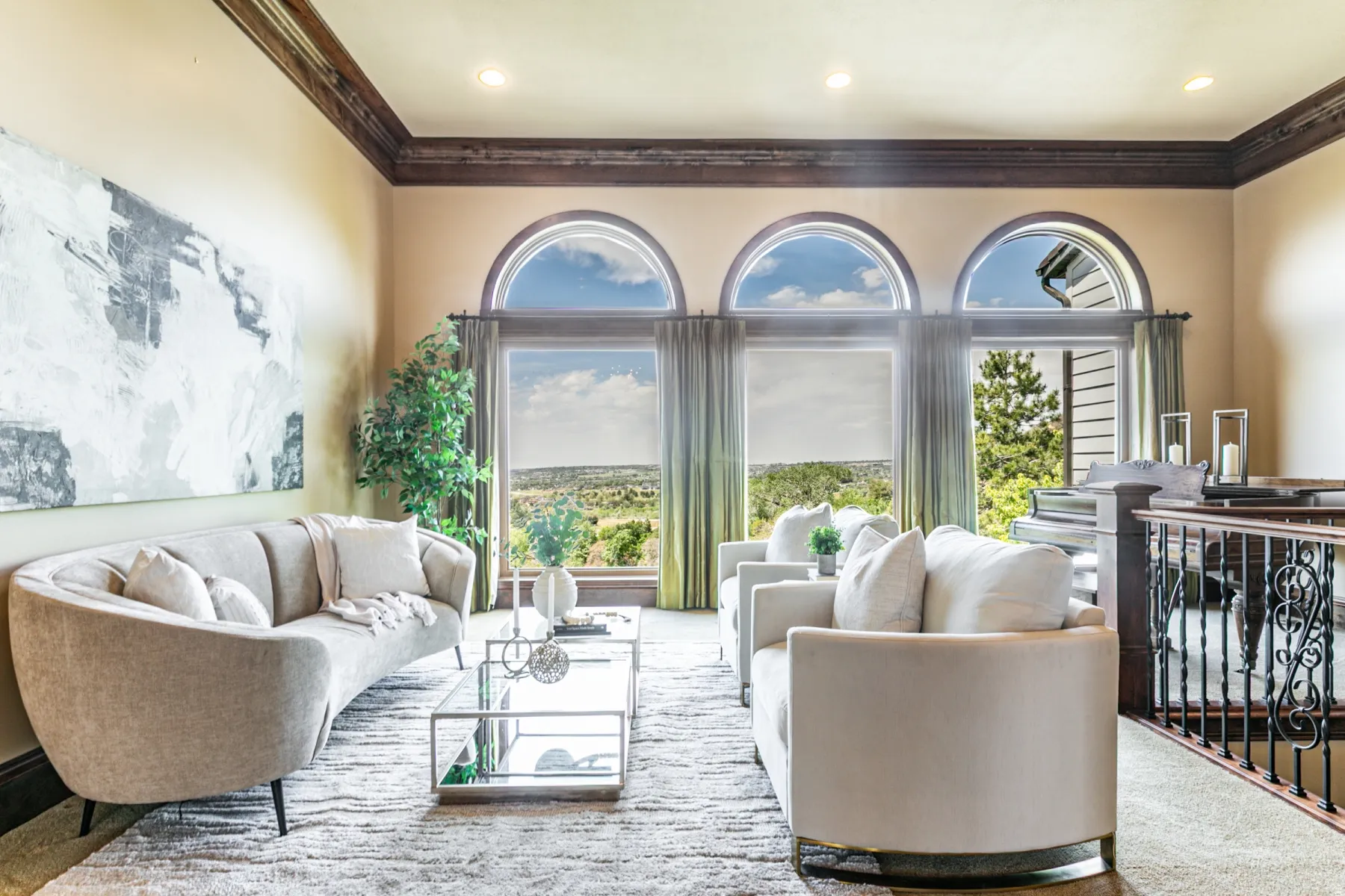 Grand living area featuring three arched windows, dark wood crown molding, recessed lighting, and a wrought iron and wood staircase railing