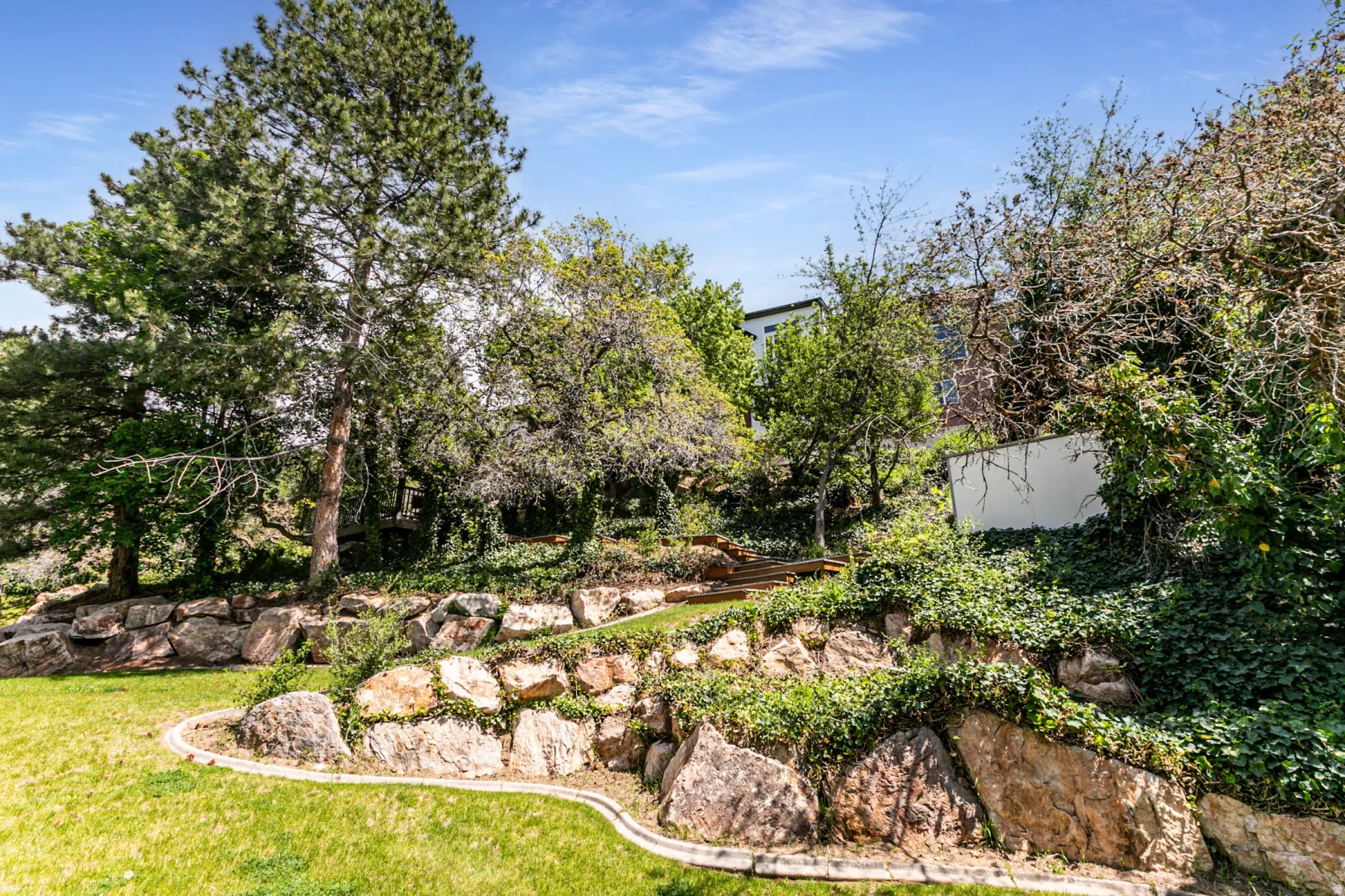 Terraced landscape featuring natural rock retaining walls, mature trees, and lush ground cover