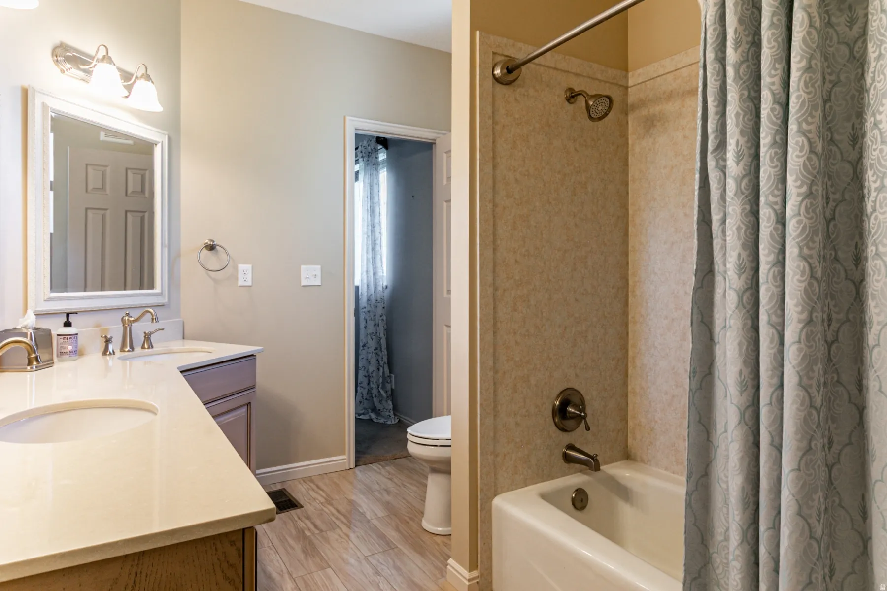 Bathroom featuring a dual vanity with light-toned countertops, a shower-over-tub combination, and wood-finish flooring