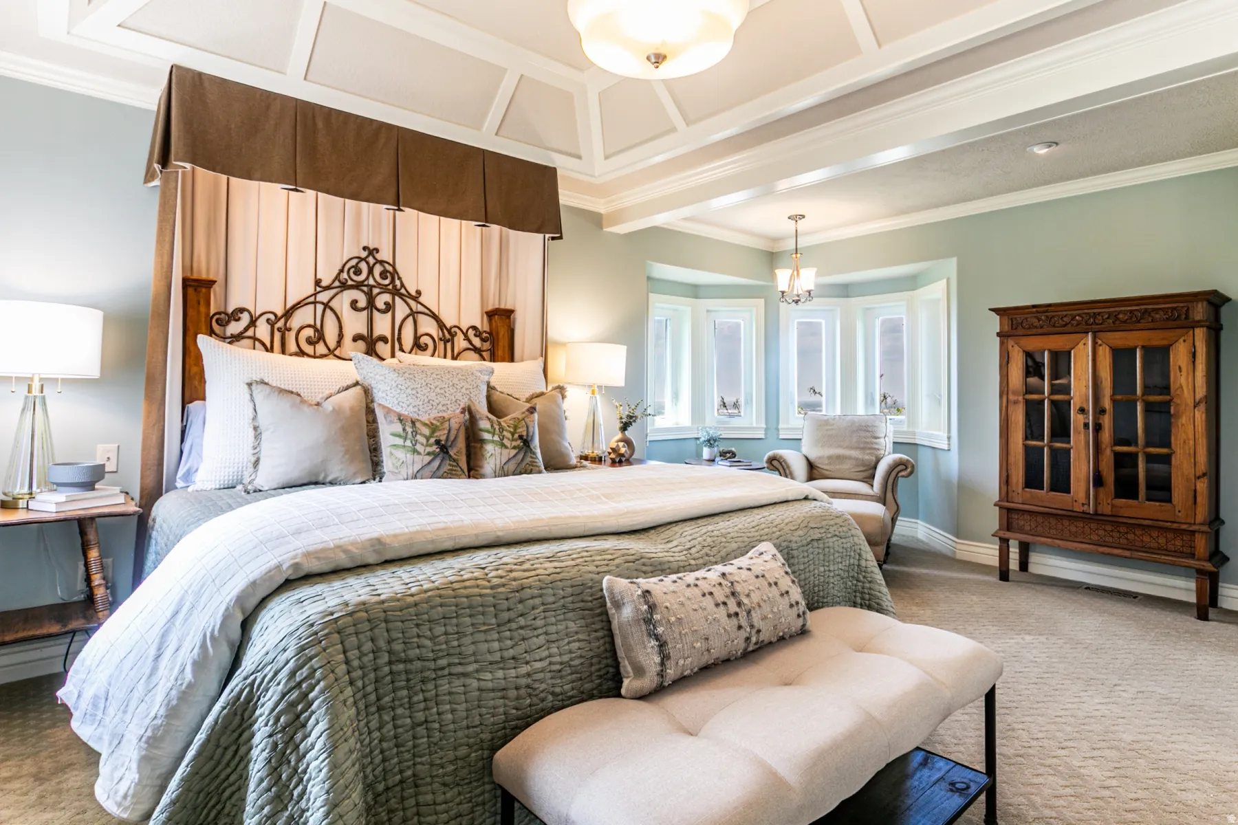 Spacious bedroom featuring an intricate coffered ceiling, light blue wall tones, and a prominent bay window with multiple panes