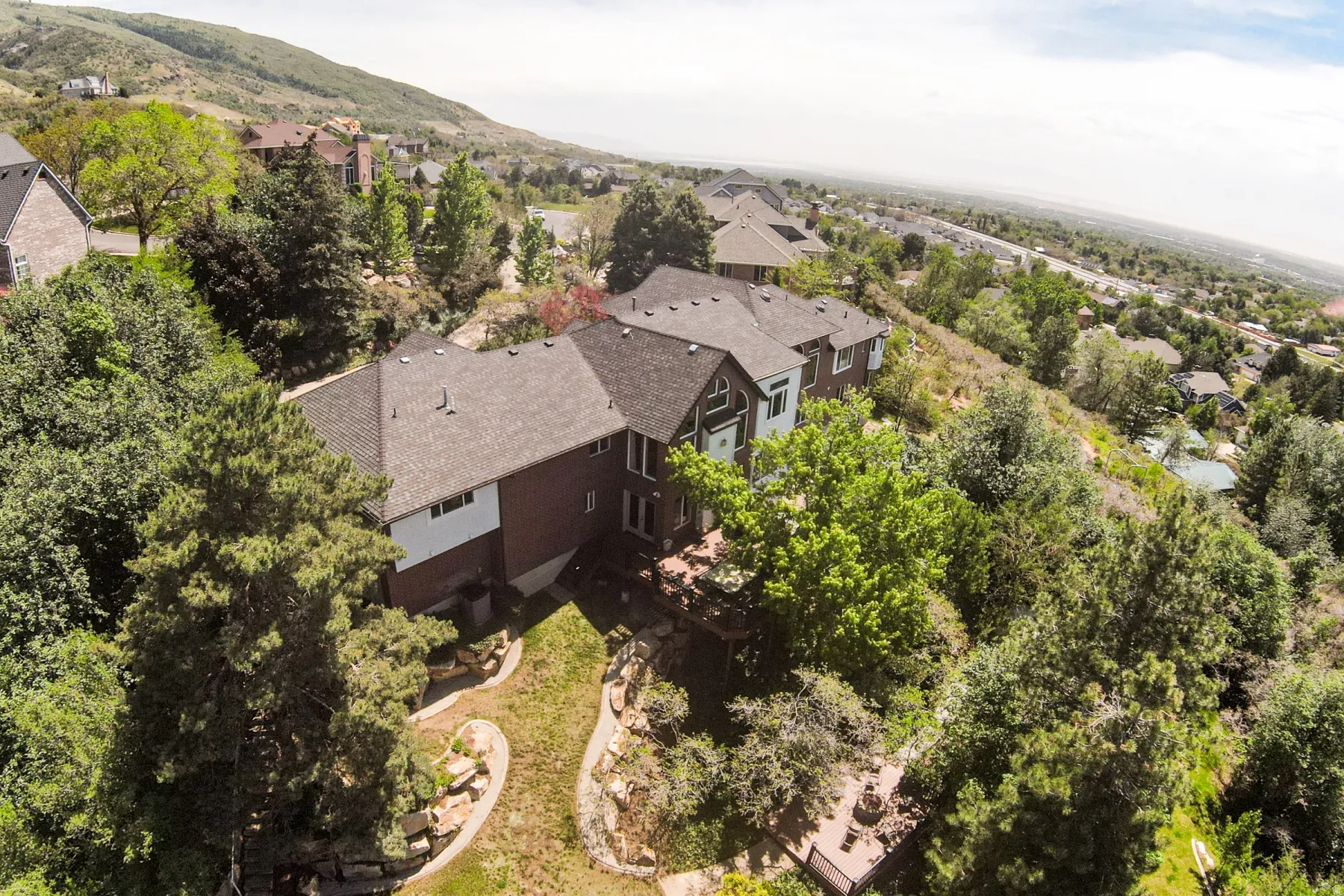 Hillside property featuring a multi-level design, a dark shingle roof, and a terraced backyard with mature trees