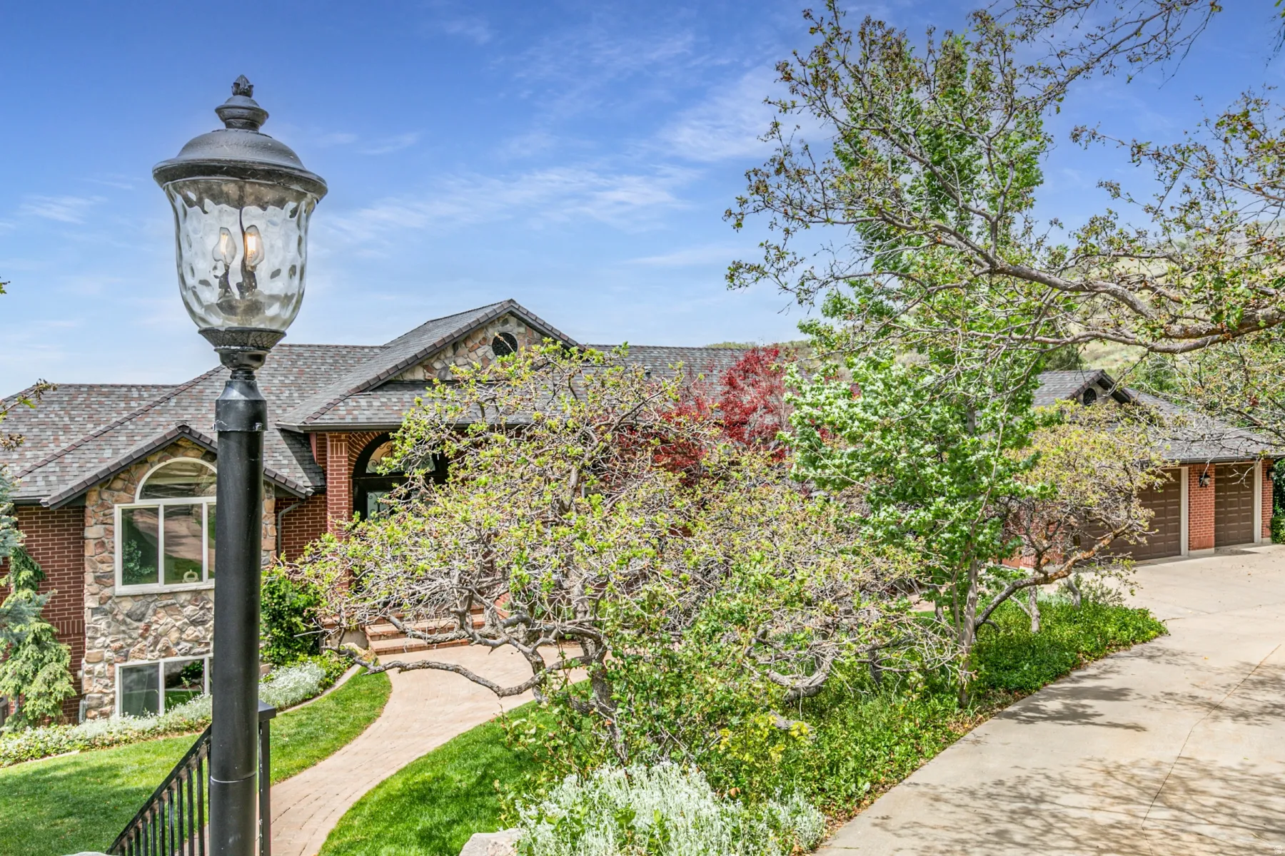 Brick and stone exterior residence featuring a prominent street lamp, arched entry, multiple windows with arch details, an attached garage, and a paved driveway