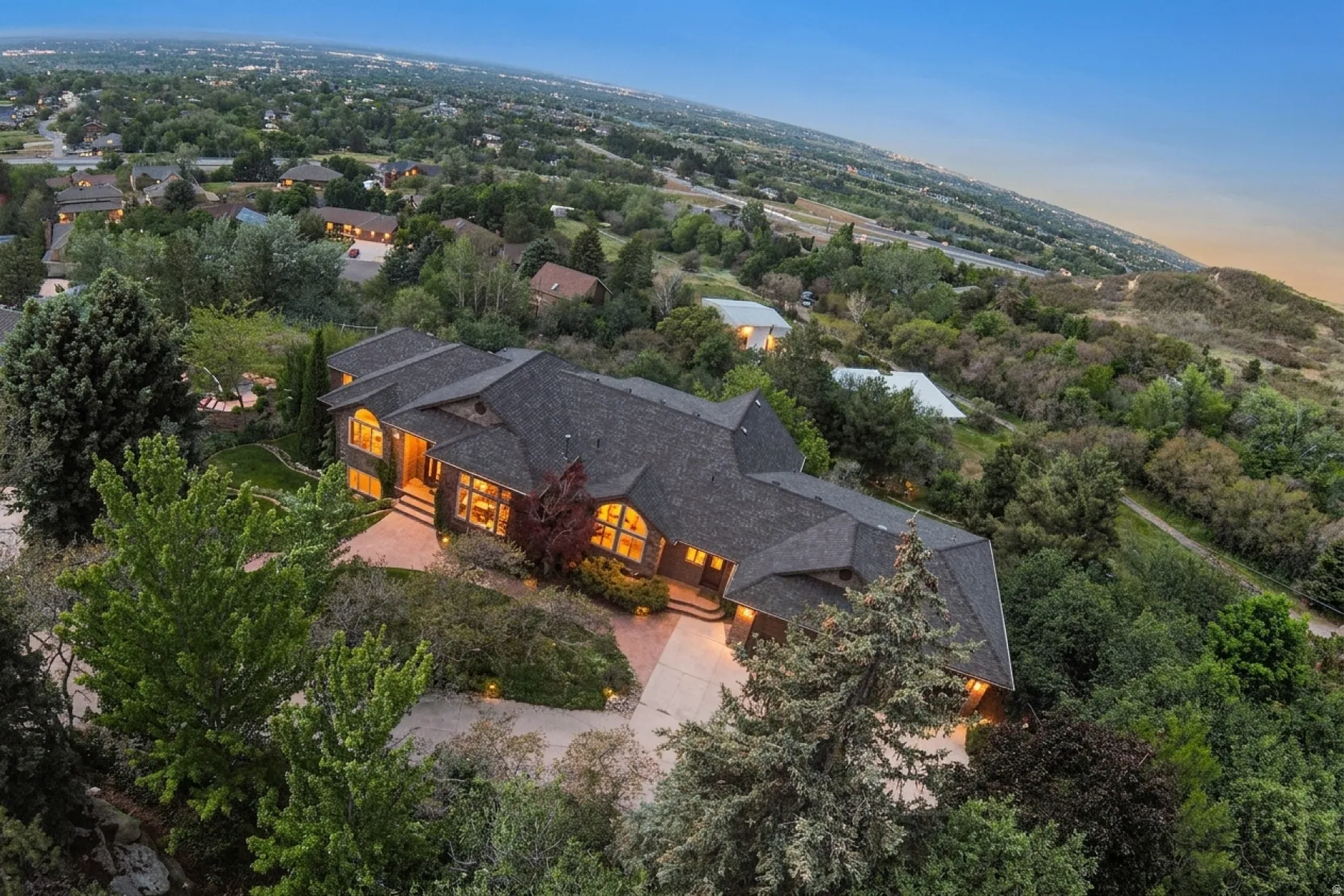 Sprawling architectural residence featuring a multi-gabled roofline, abundant mature landscaping, and an extensive paved drive