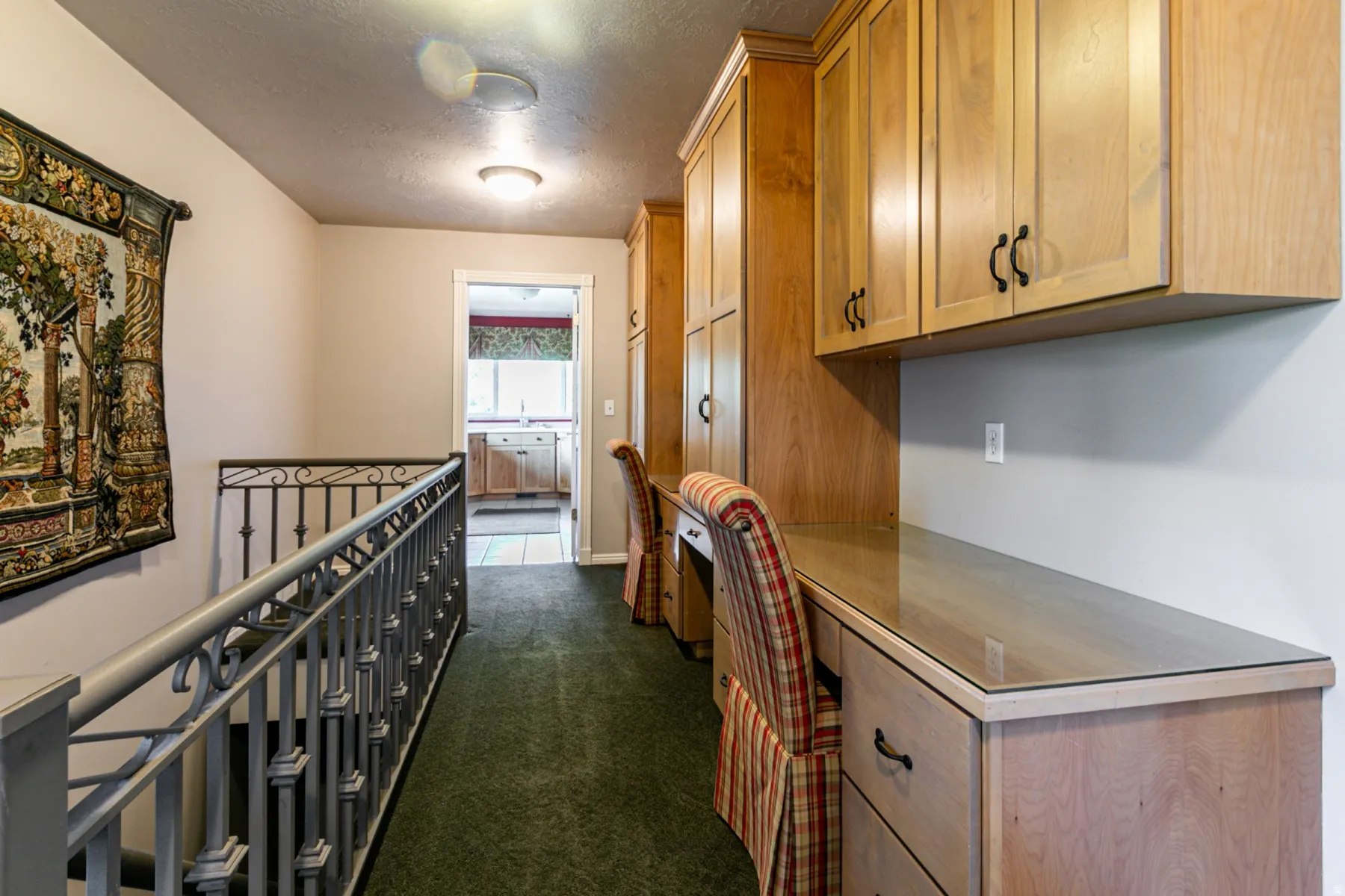 Hallway featuring built-in wood cabinetry with black hardware, integrated desk space with glass tops, and dark green carpeting