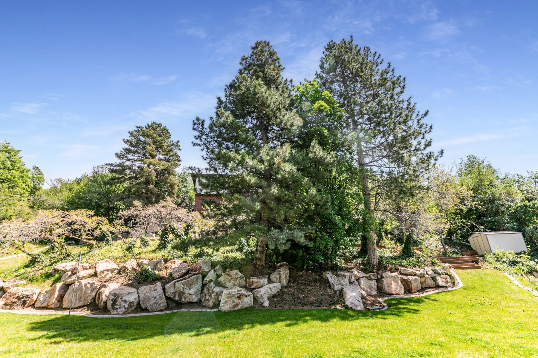 Grassed lawn area with a natural rock retaining wall, mature trees, and tiered landscaping