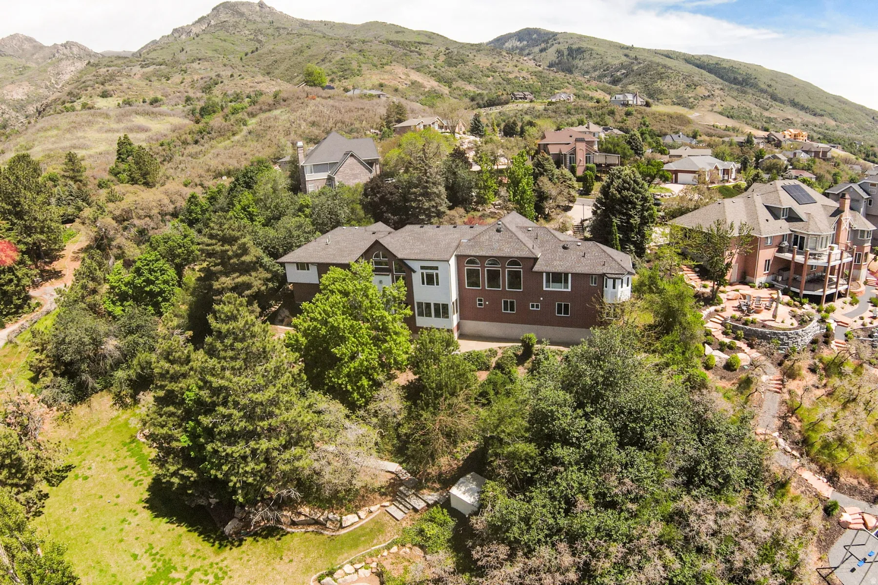 Terraced hillside property featuring a multi-story residence with a pitched roof, a brown brick facade, a white siding section, and multiple windows