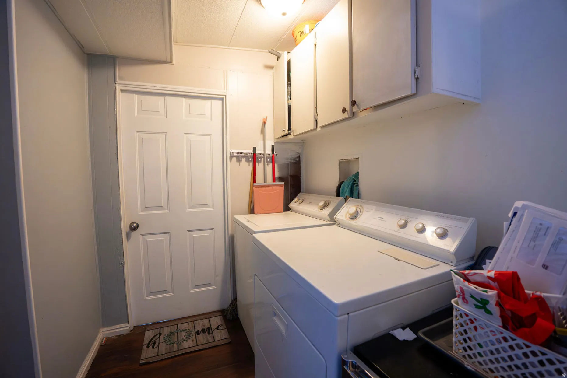 Dedicated laundry area featuring overhead cabinetry, wood-finish flooring, and a paneled door