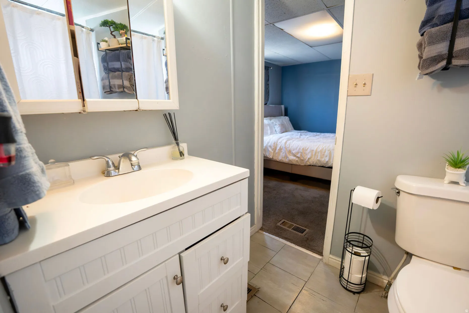 Bathroom featuring a white vanity with beadboard paneling, integrated sink, chrome faucet, and a tri-fold medicine cabinet