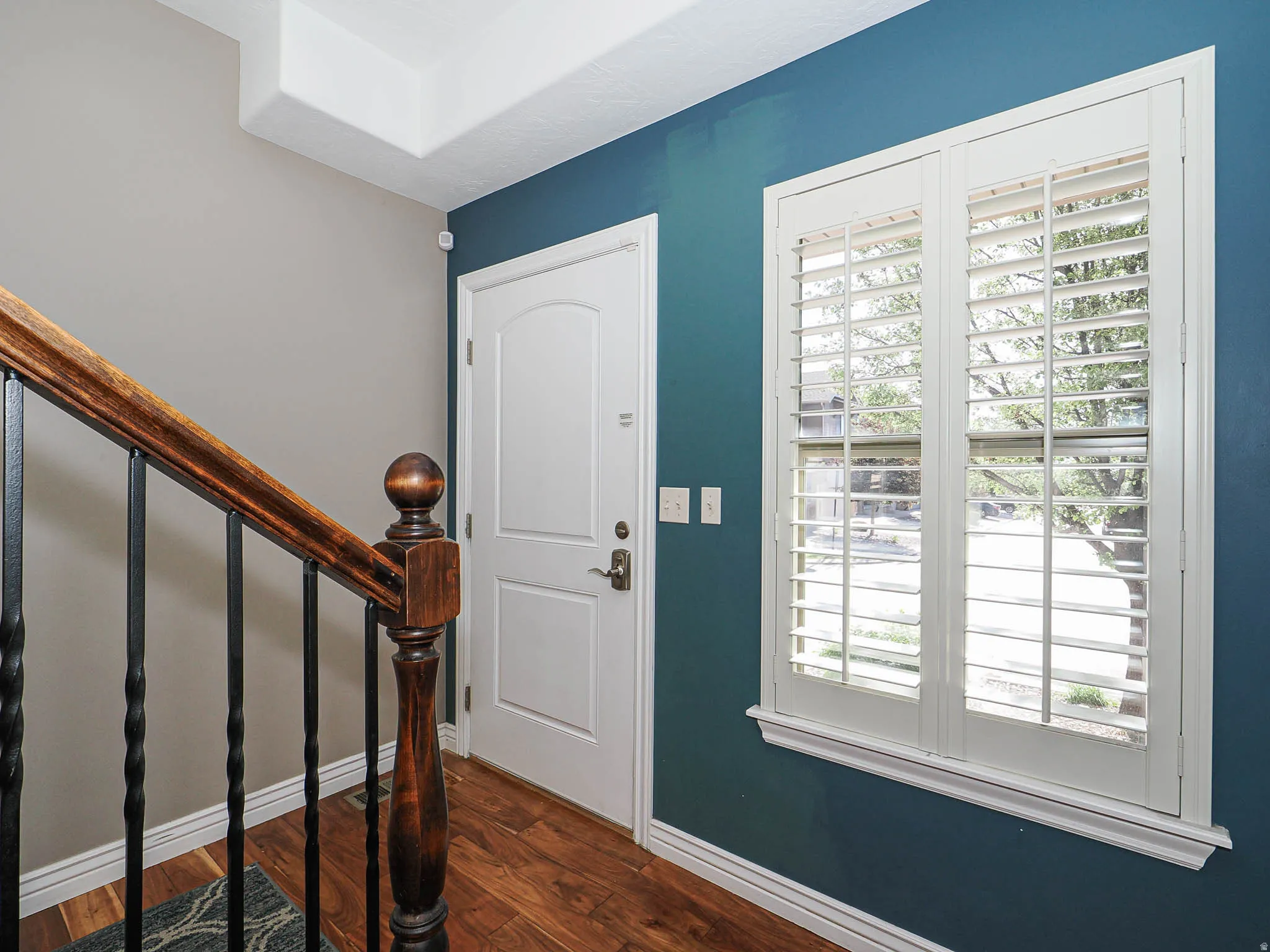 Entryway featuring rich wood-finish flooring, a solid white paneled entry door, and a staircase with a carved wood-finish handrail and black iron balusters