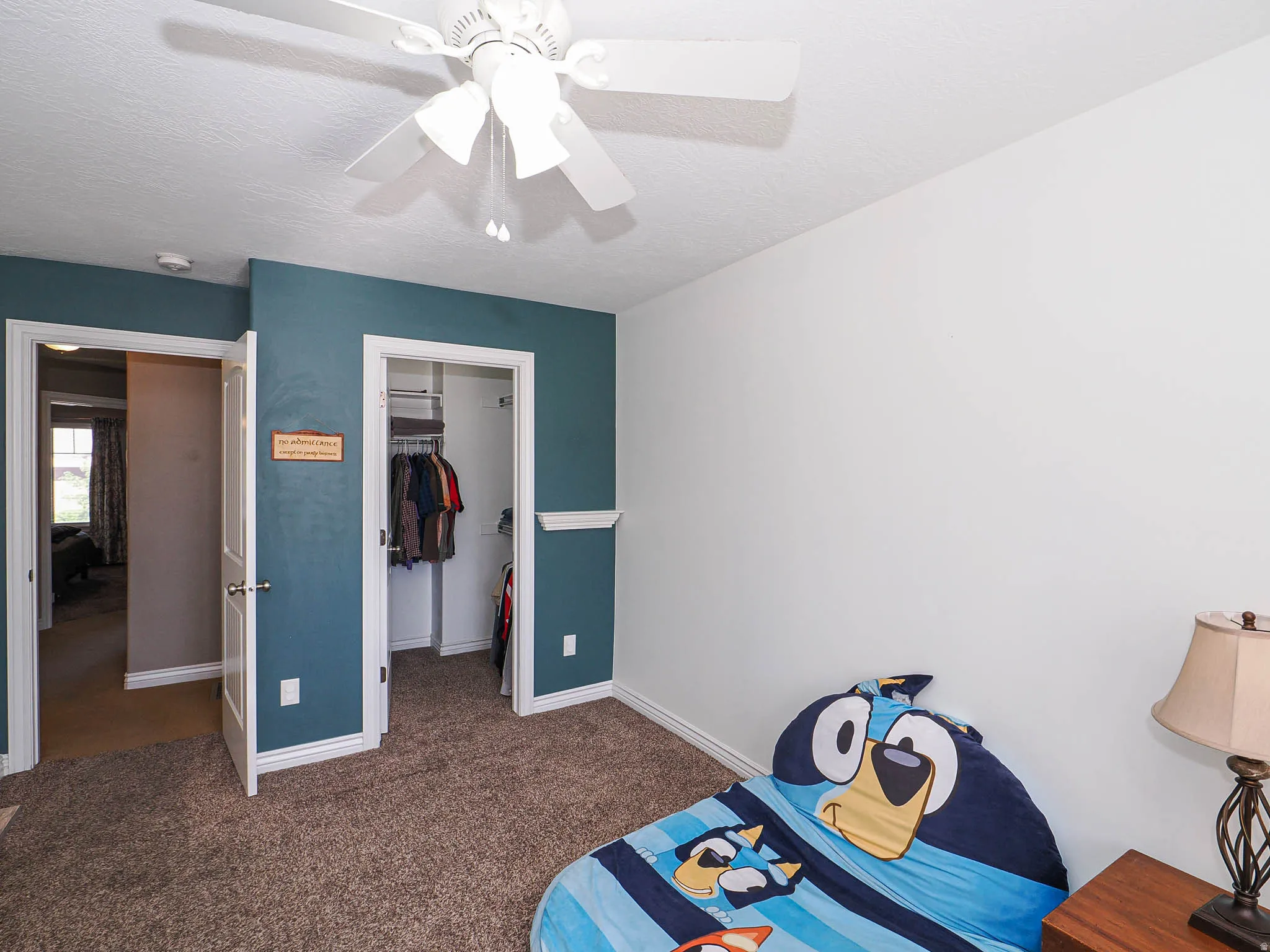 Carpeted room featuring a ceiling fan, white trim, and a built-in closet with shelving and hanging storage