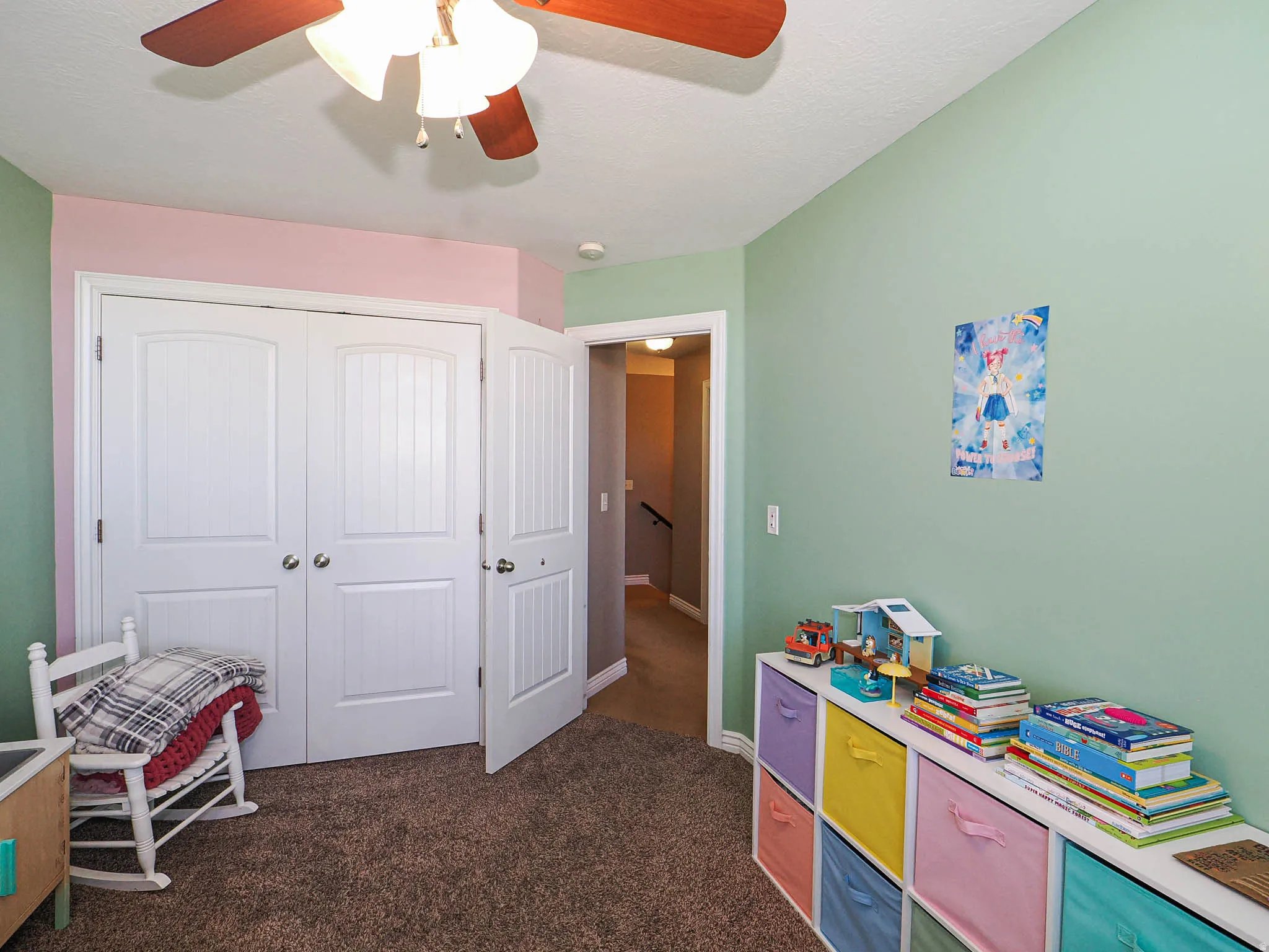Room featuring textured carpet flooring, a ceiling fan with light fixture, and a dual-door closet with paneled doors