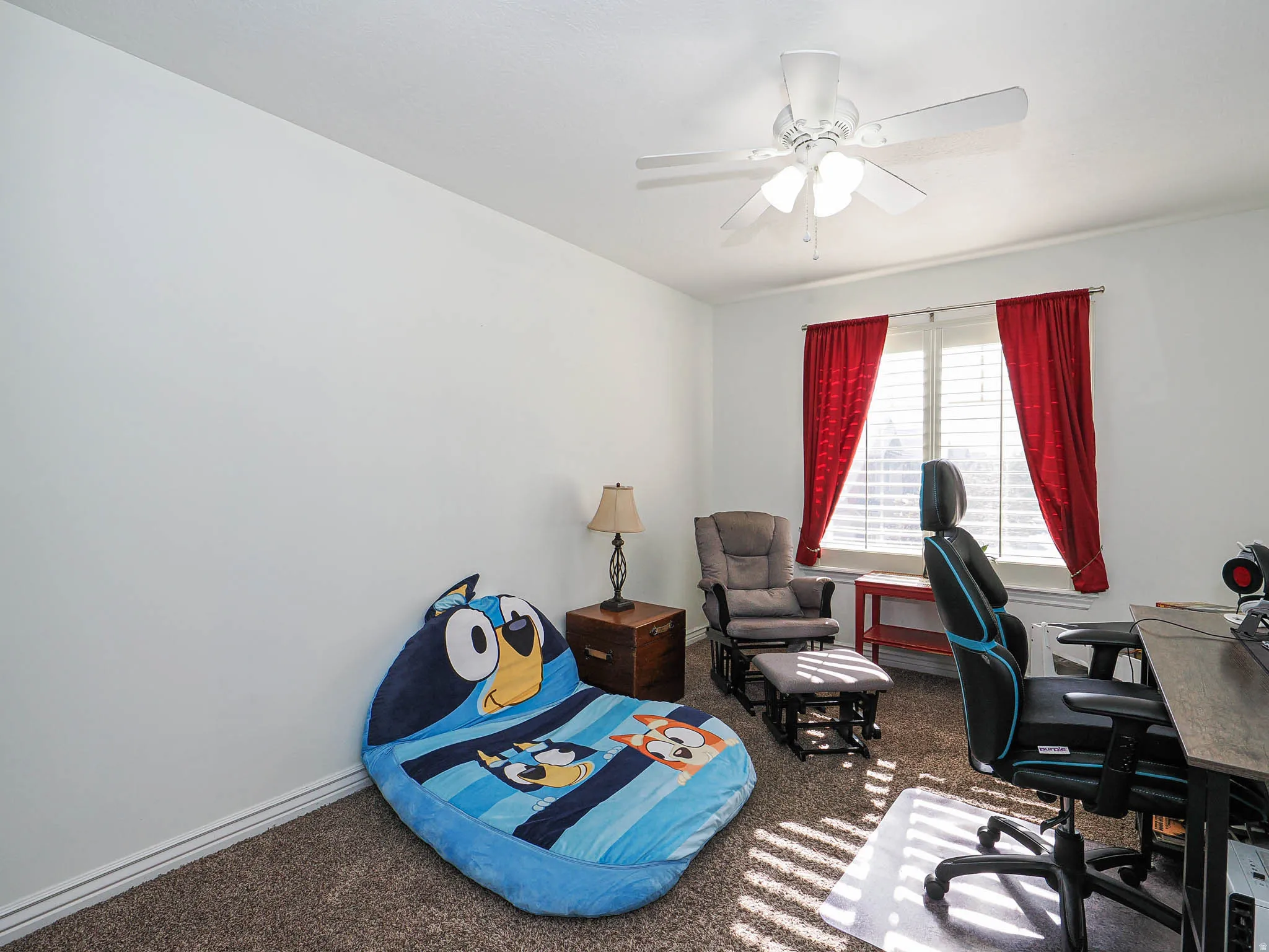 Room featuring a window with white shutters and red drapery, carpet flooring, baseboard molding, and a ceiling fan with light fixture