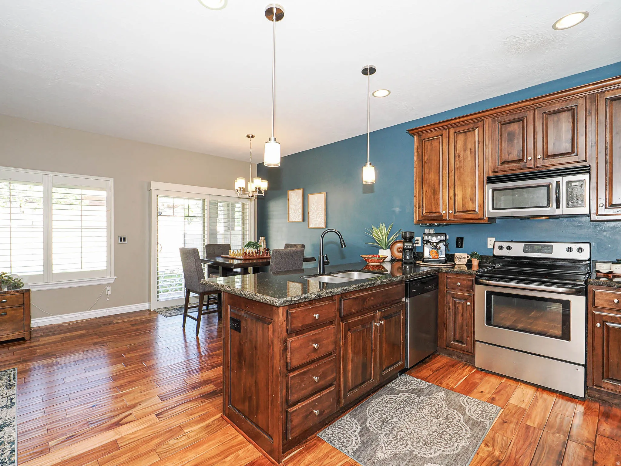 Kitchen featuring wood-finish flooring, dark wood cabinetry, stainless steel appliances, and a central island with a granite countertop and integrated sink