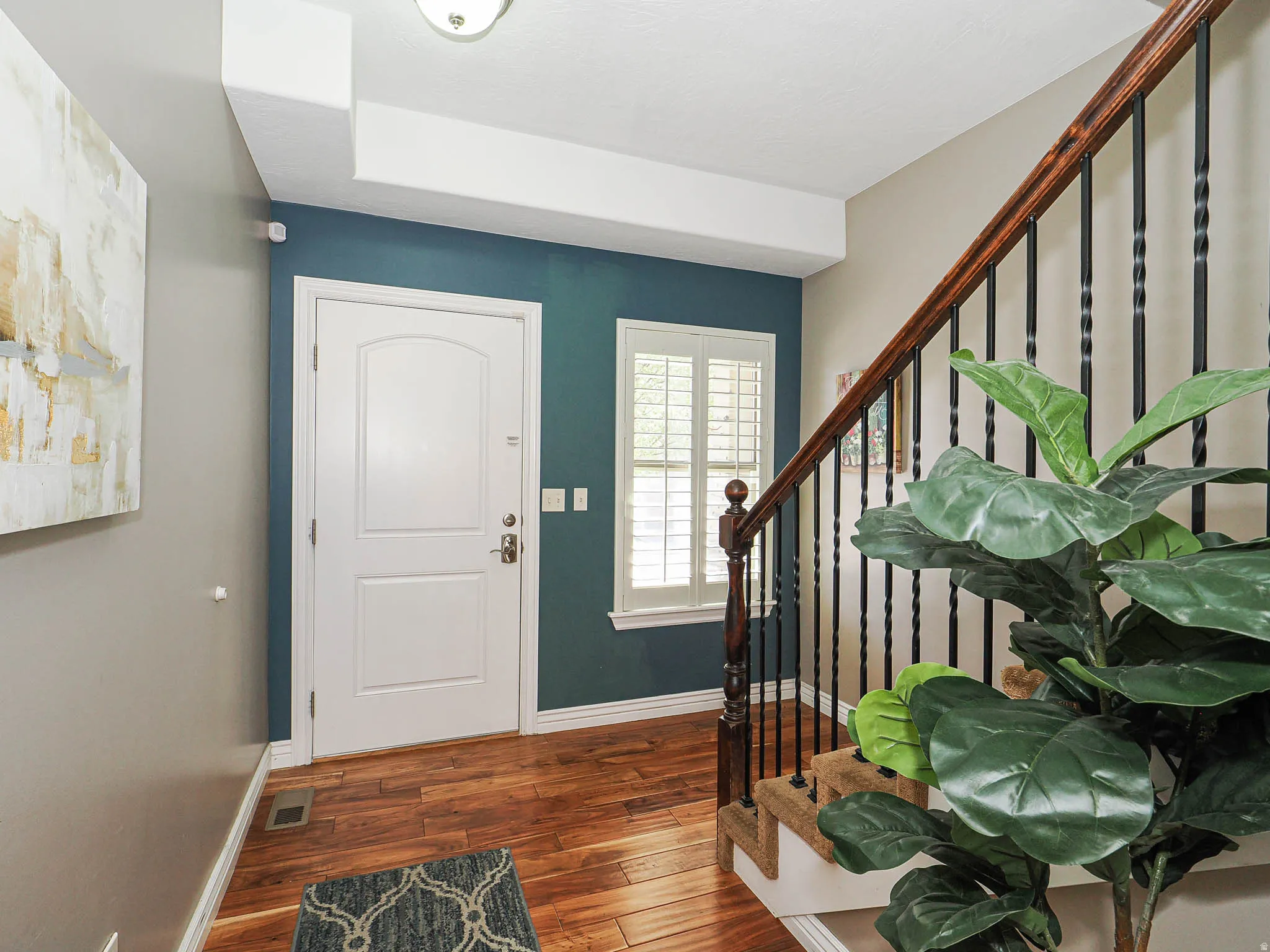 Entryway featuring wood-finish flooring, a white paneled front door, and a staircase with dark wood handrails and black metal balusters