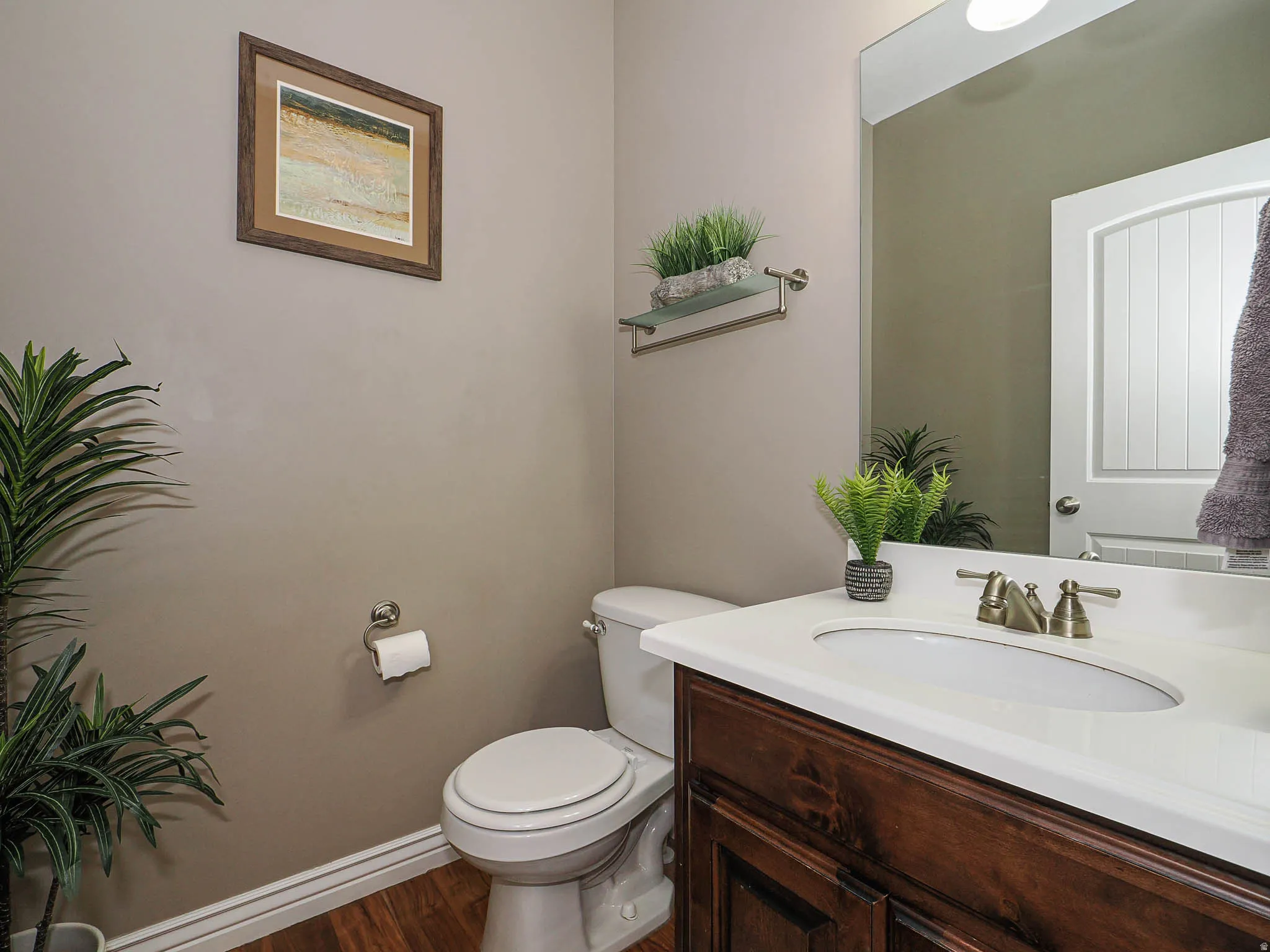 Powder room featuring a wood-finish vanity with a white countertop and undermount sink, brushed brass faucet, framed mirror, and wood-finish flooring