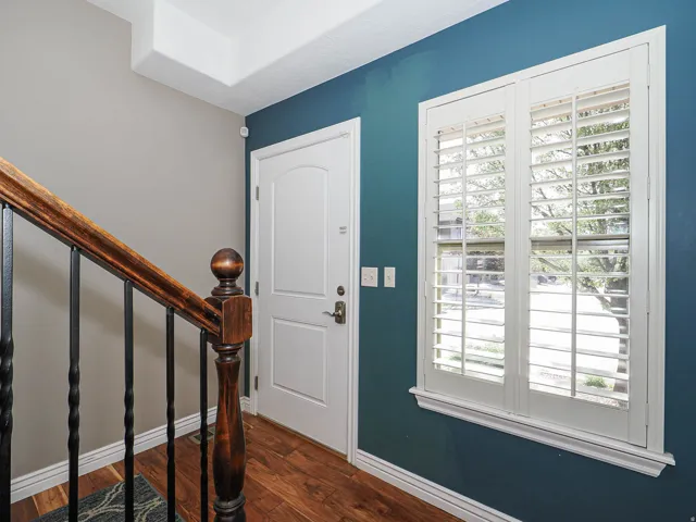 Entryway featuring rich wood-finish flooring, a solid white paneled entry door, and a staircase with a carved wood-finish handrail and black iron balusters