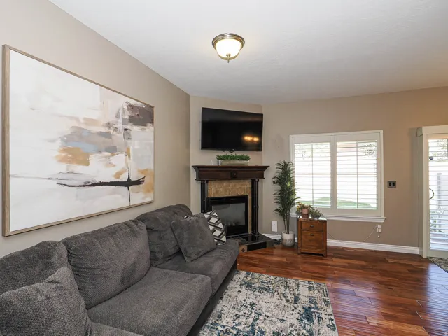 Living area featuring wood-finish flooring, a corner fireplace with a dark wood mantel and tile surround, and a window with plantation shutters