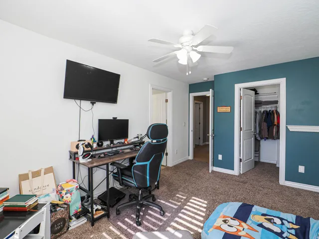 Carpeted room with a ceiling fan, a wall-mounted television, and a built-in closet with bifold doors