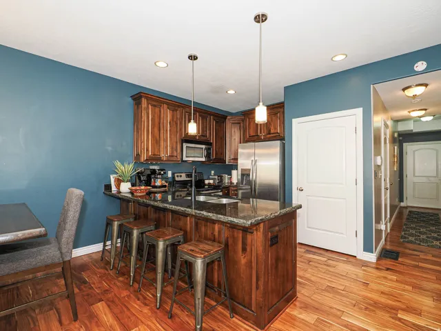 Kitchen featuring warm wood cabinetry, dark speckled countertops, stainless steel appliances, and wood-finish flooring