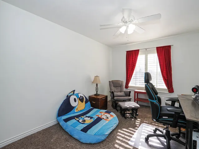 Room featuring a window with white shutters and red drapery, carpet flooring, baseboard molding, and a ceiling fan with light fixture