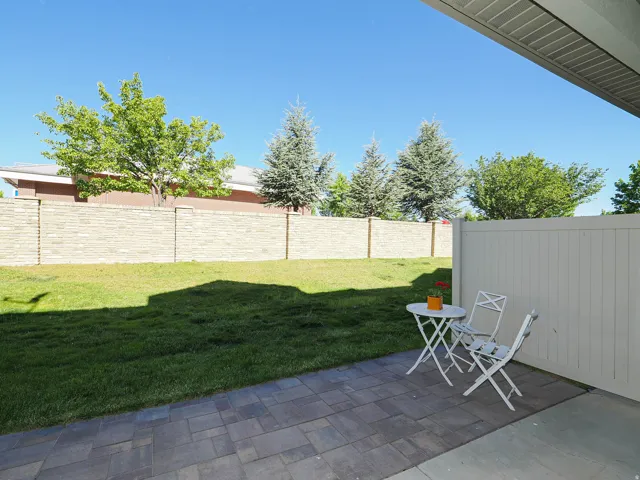 Expansive paver patio with a white privacy fence and a manicured lawn