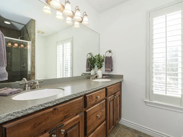 Double vanity with under-mount sinks, a textured stone countertop, and wood-finish cabinetry