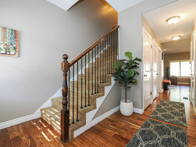 Entryway featuring wood-finish flooring, a carpeted staircase with wood banister and wrought iron spindles, and ceiling-mounted light fixtures