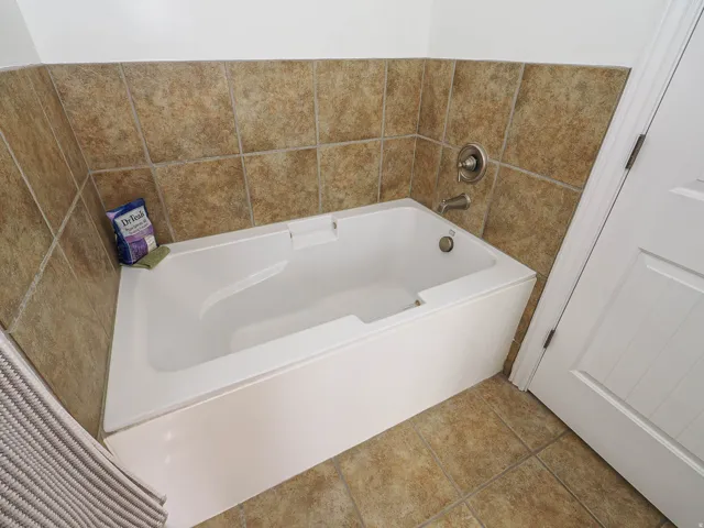 White soaking tub with brushed nickel fixtures, surrounded by neutral-toned tiled walls and flooring