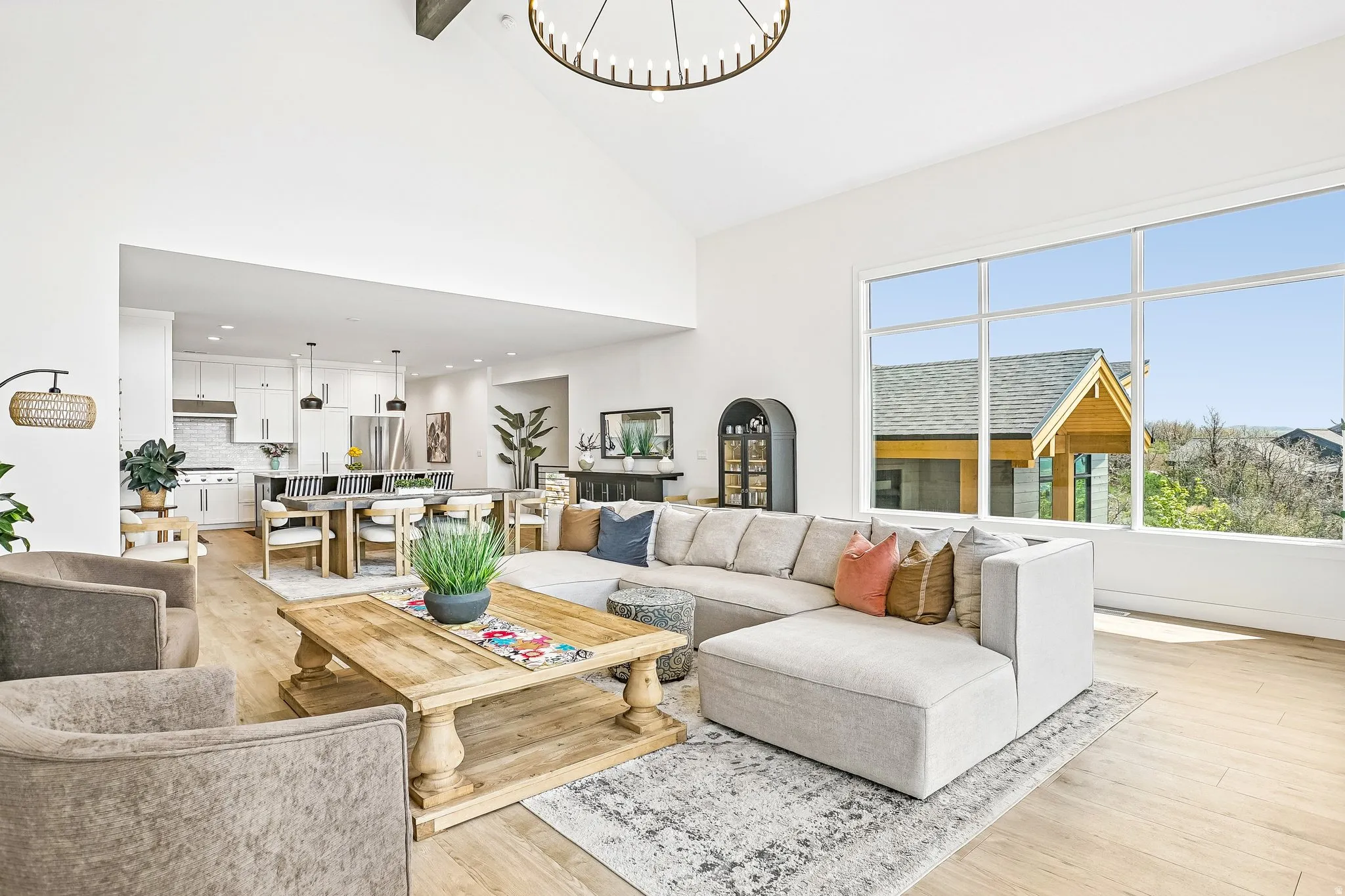 Bright living area featuring a vaulted ceiling with exposed beam, large picture windows, wood-finish flooring, and a contemporary chandelier