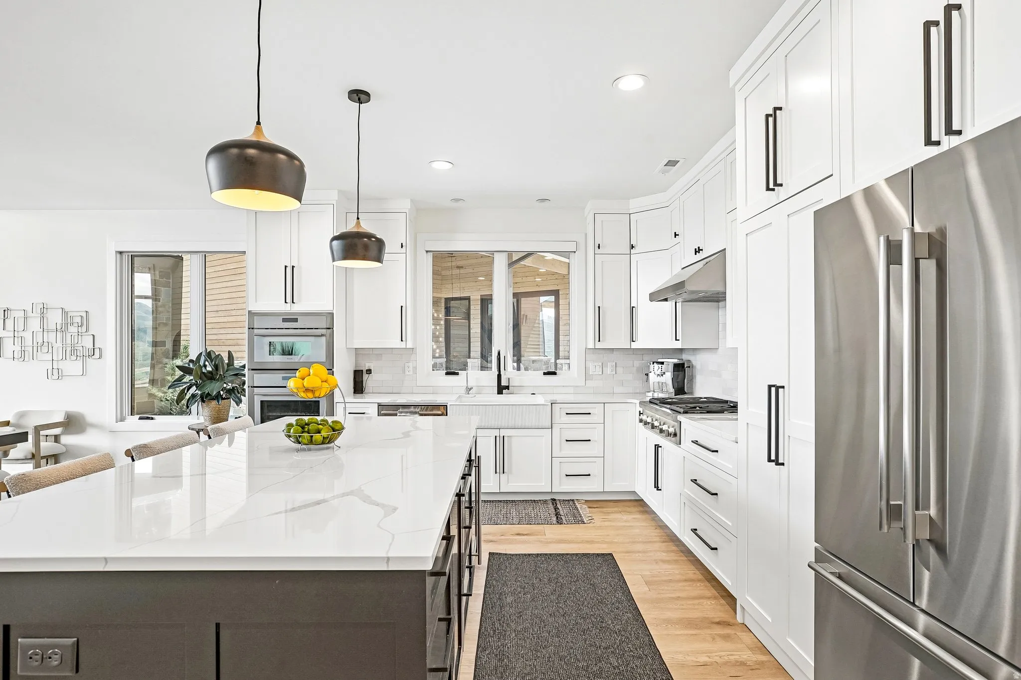 Gourmet kitchen featuring a large central island with seating, white shaker cabinetry, stainless steel appliances, and wood-finish flooring