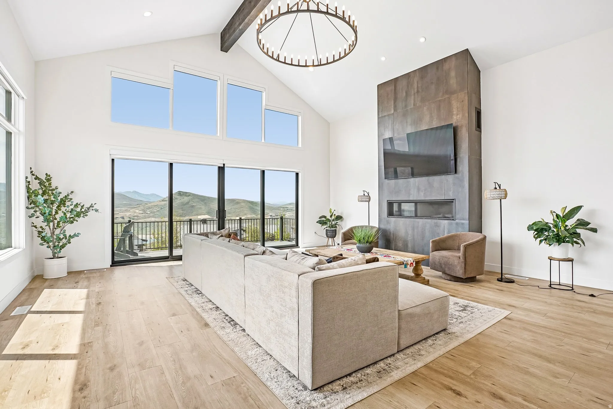 Vaulted living space featuring a floor-to-ceiling fireplace with dark paneling, wide plank wood-finish flooring, and expansive windows showcasing mountain scenery