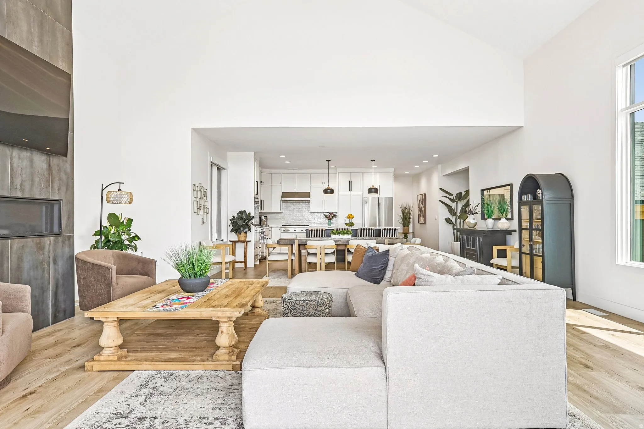 Spacious living area featuring high vaulted ceilings, light wood-finish flooring, and a contemporary linear fireplace with a textured surround