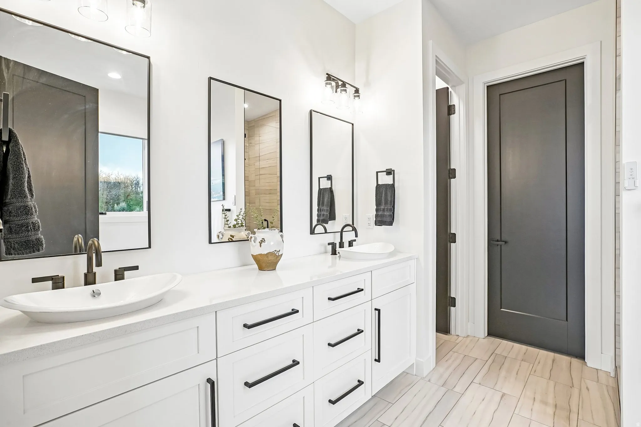 Dual vanity with white cabinetry and matte black hardware, white vessel sinks with wall-mounted bronze-finish faucets, framed mirrors, and wood-finish flooring