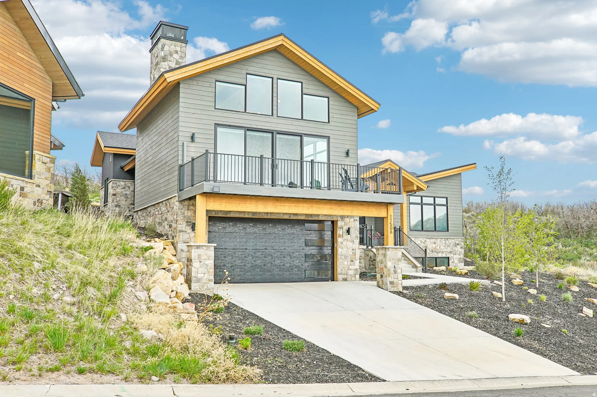 Modern architectural design featuring gray horizontal siding, stone accents, and a prominent balcony with metal railings