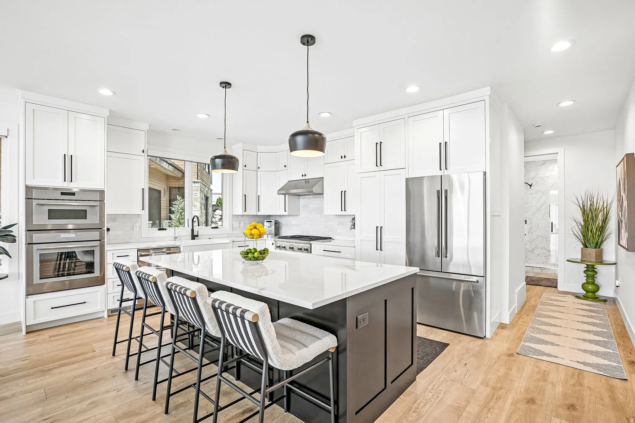Spacious kitchen featuring an expansive island with seating, white shaker cabinetry, stainless steel appliances, and wood-finish flooring