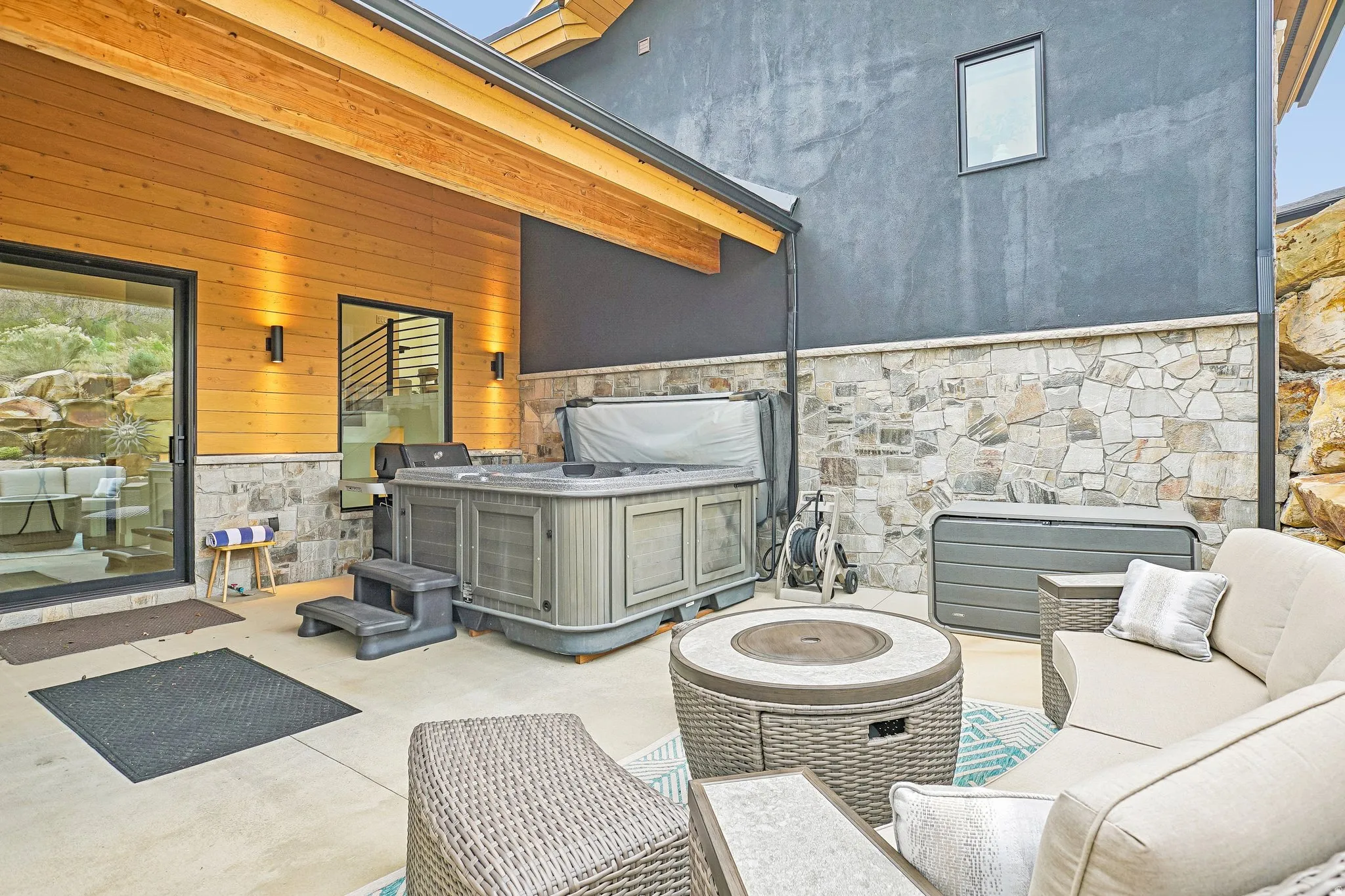 Outdoor patio featuring a hot tub, concrete flooring, and a stone veneer wall base