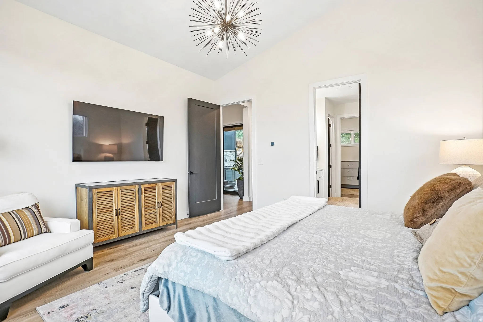 Vaulted ceiling with a contemporary chandelier, wood-finish flooring, two panel interior doors, and a built-in wall-mounted television