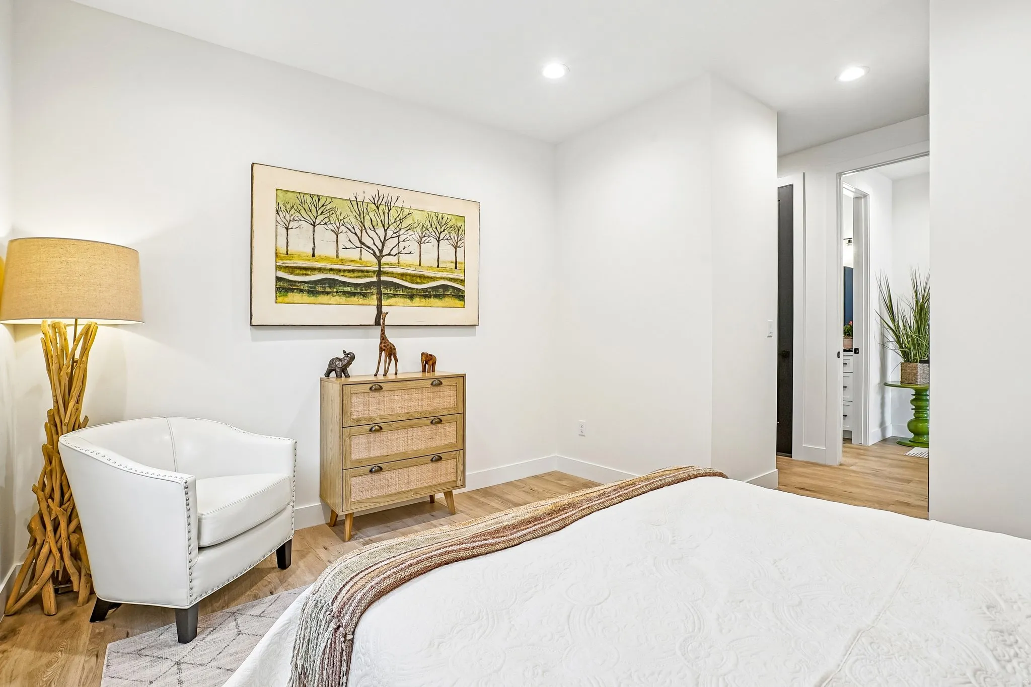 Light wood-finish flooring throughout, featuring recessed lighting, white painted walls, and a doorway leading to an additional space