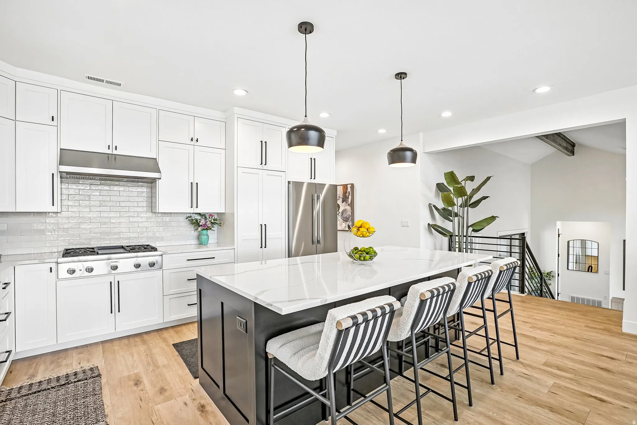 Spacious kitchen featuring an oversized island with countertop seating, stainless steel appliances, white subway tile backsplash, and light wood-finish flooring