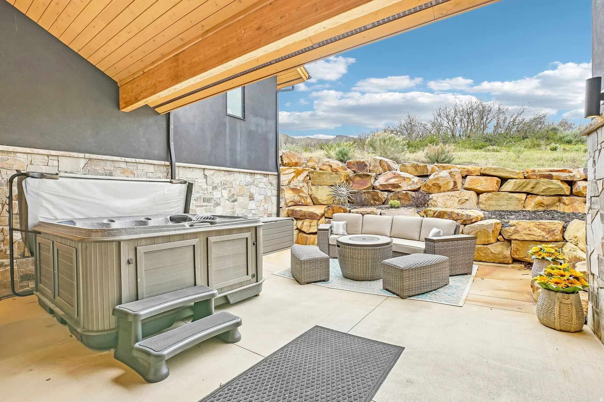 Covered patio featuring a built-in spa, concrete flooring, and a stacked stone retaining wall