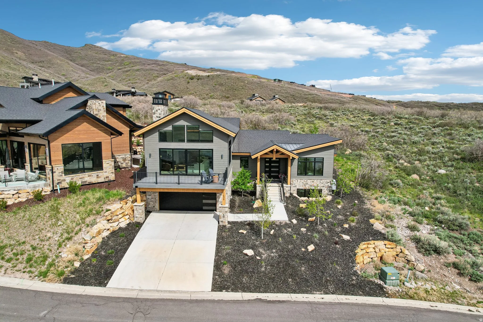 Contemporary mountain-style home featuring a two-car garage, upper-level balcony, and a multi-level stone and wood-look exterior