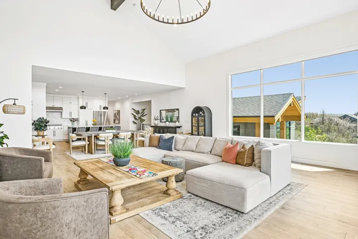 Bright living area featuring a vaulted ceiling with exposed beam, large picture windows, wood-finish flooring, and a contemporary chandelier