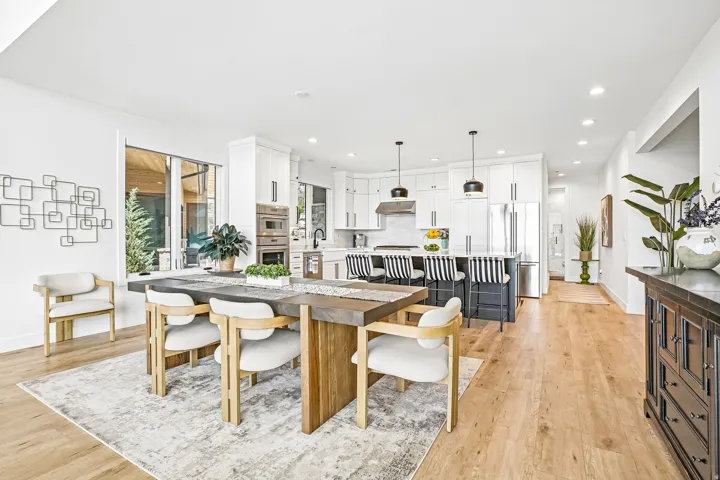 Open-concept kitchen and dining area featuring light wood-finish flooring, white cabinetry, stainless steel appliances, a center island with pendant lighting, and abundant natural light from large windows