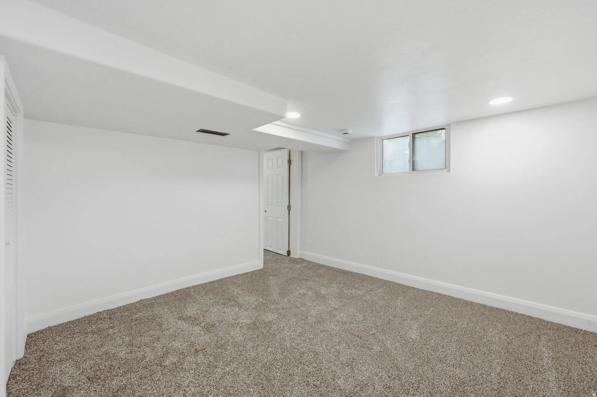 Spacious room featuring neutral carpeting, white walls, recessed lighting, and a white interior door
